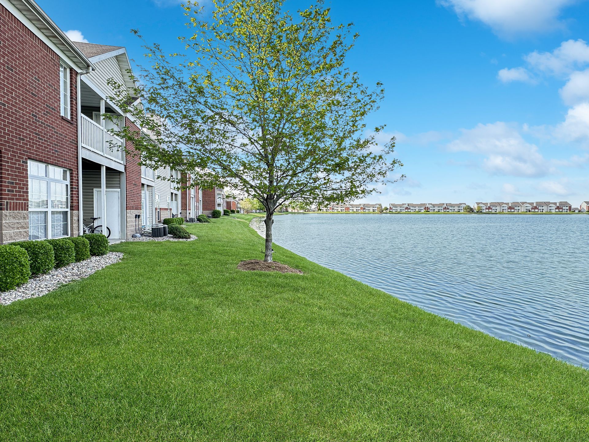 Apartment complex with brick exterior beside a lake on a sunny day.