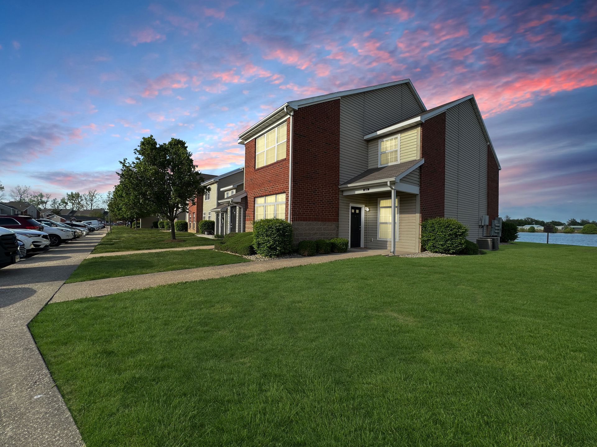 Two-story apartment building with brick accents, green lawn, and cloudy sky.