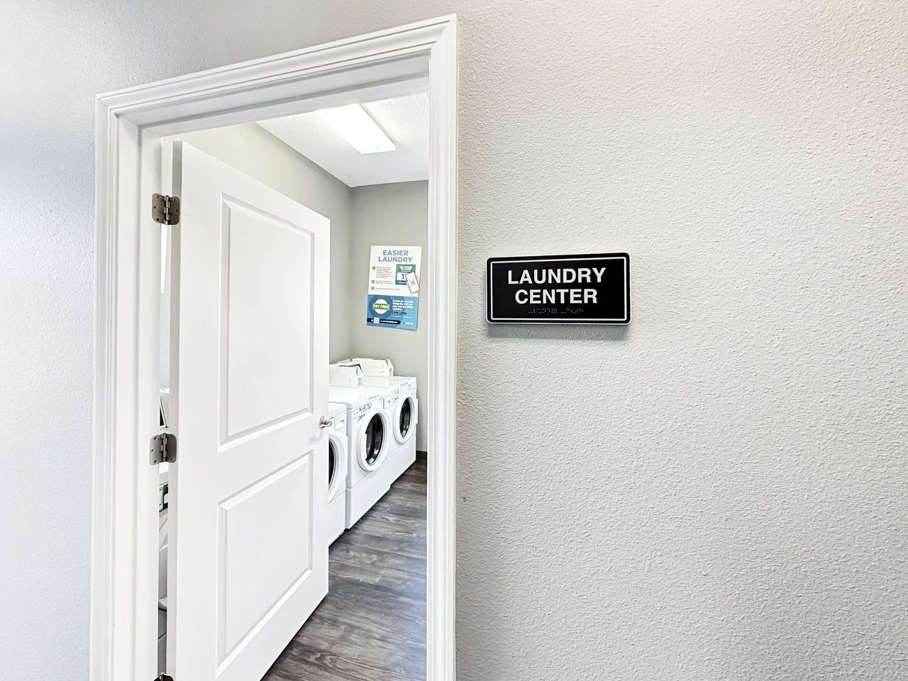 Open door to laundry center with washing machines. Sign on the wall reads