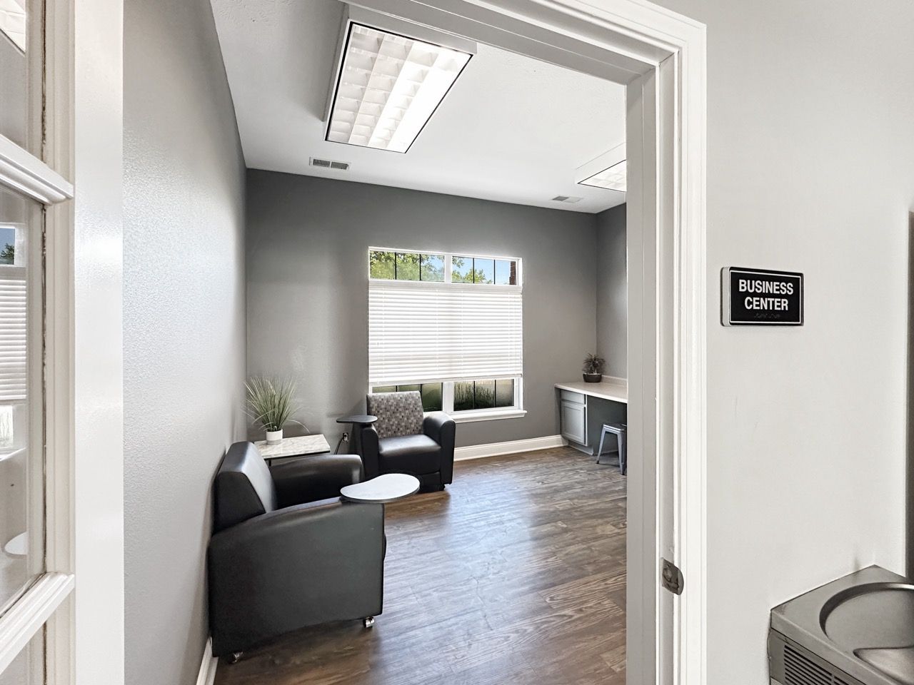 Interior view of a waiting room with gray walls, two black chairs, and a desk.