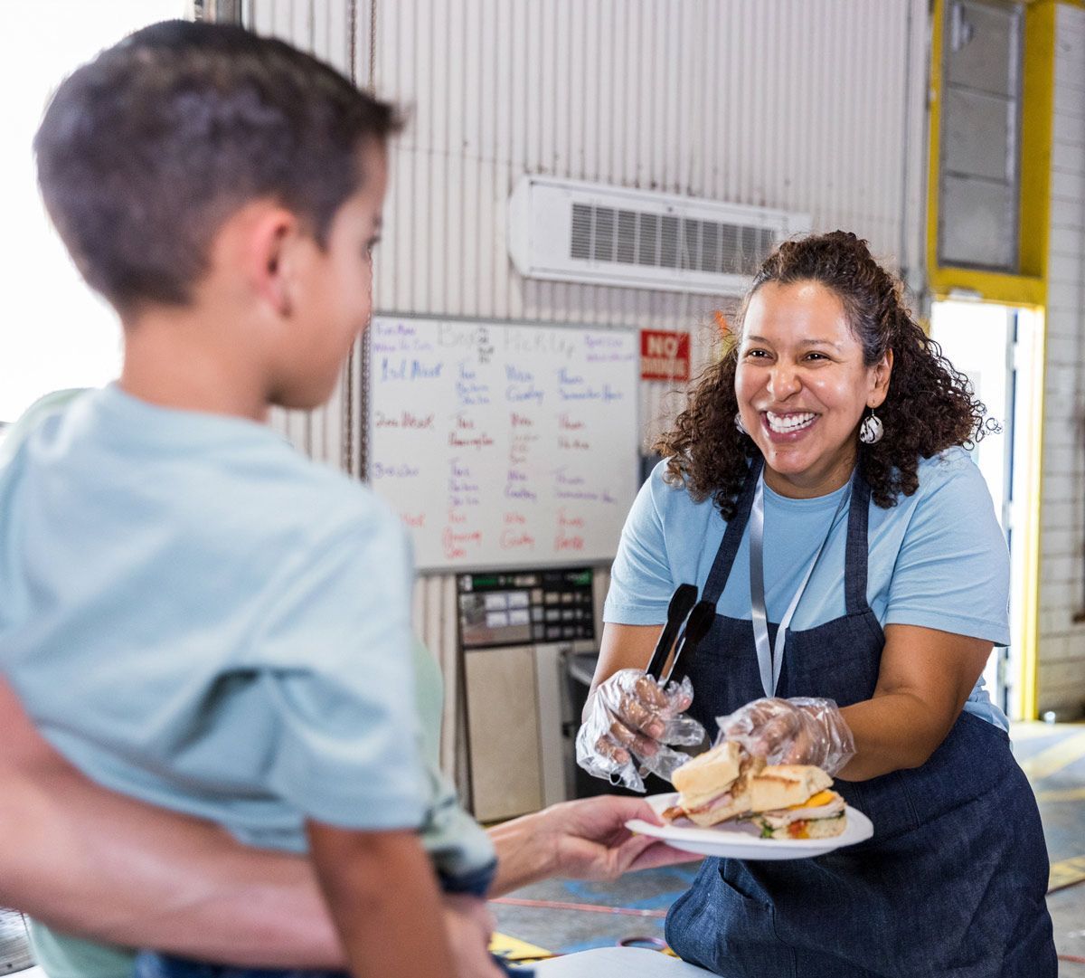 A woman is serving a plate of food to a young boy