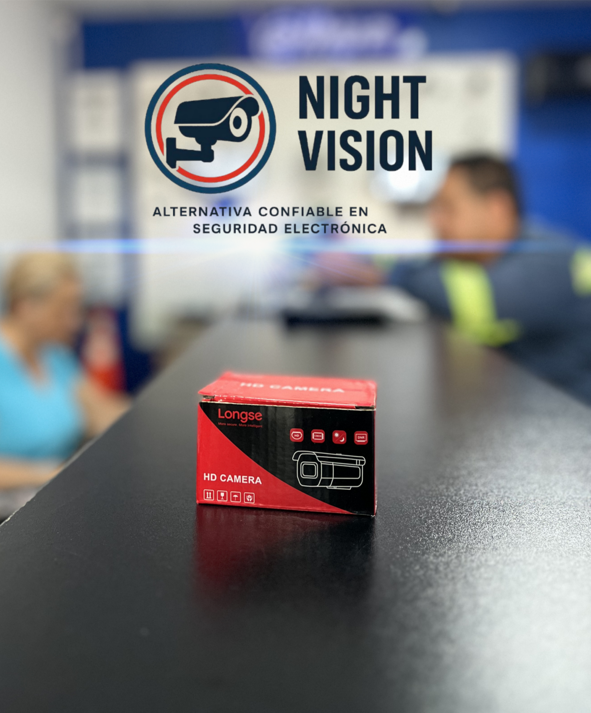 Caja roja de producto sobre un mostrador con el logo de "Visión Nocturna" al fondo. Dos personas borrosas al fondo.