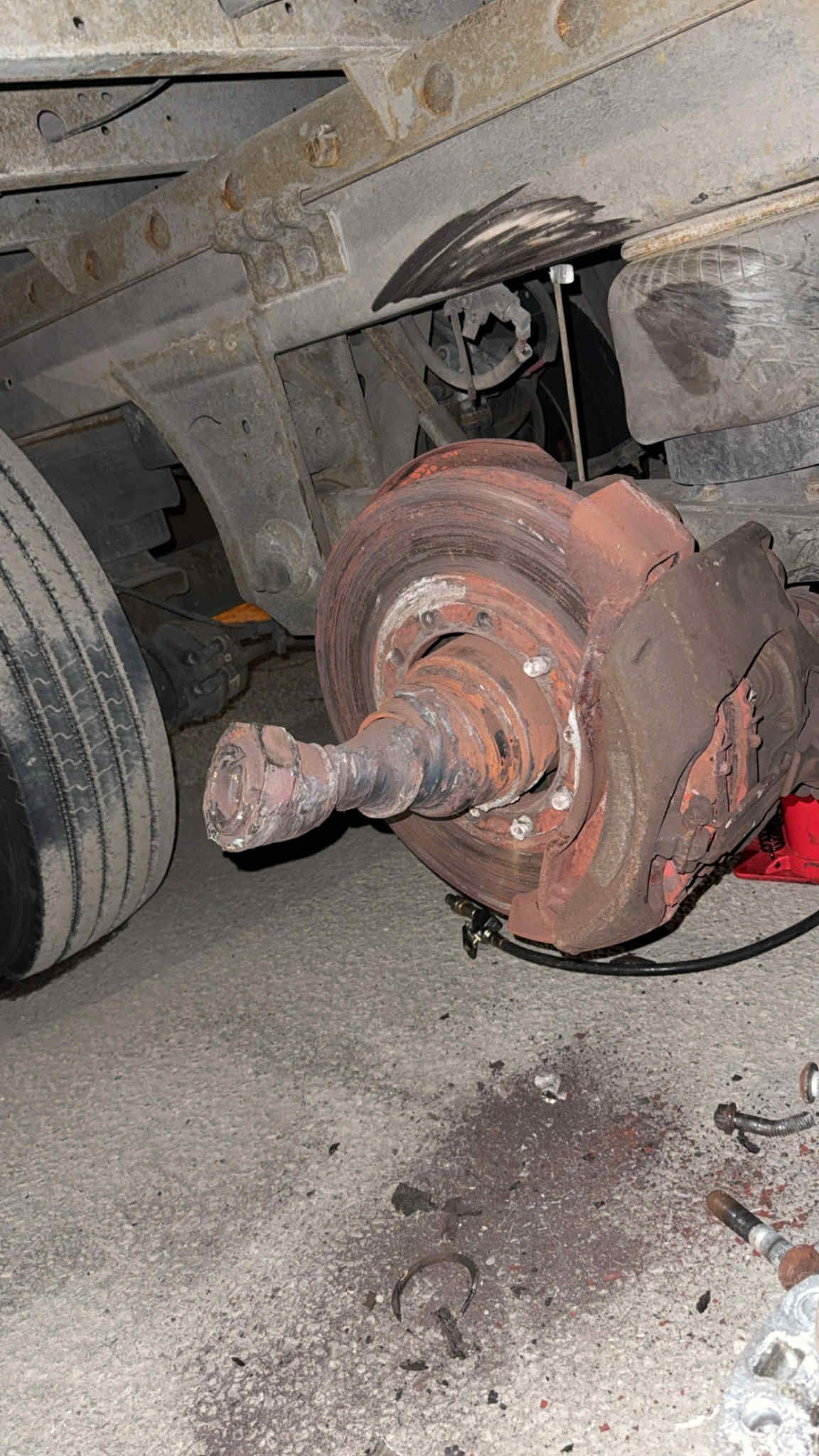 A close-up view of a vehicle's rusted brake rotor and axle assembly, with a detached tire visible on the left.