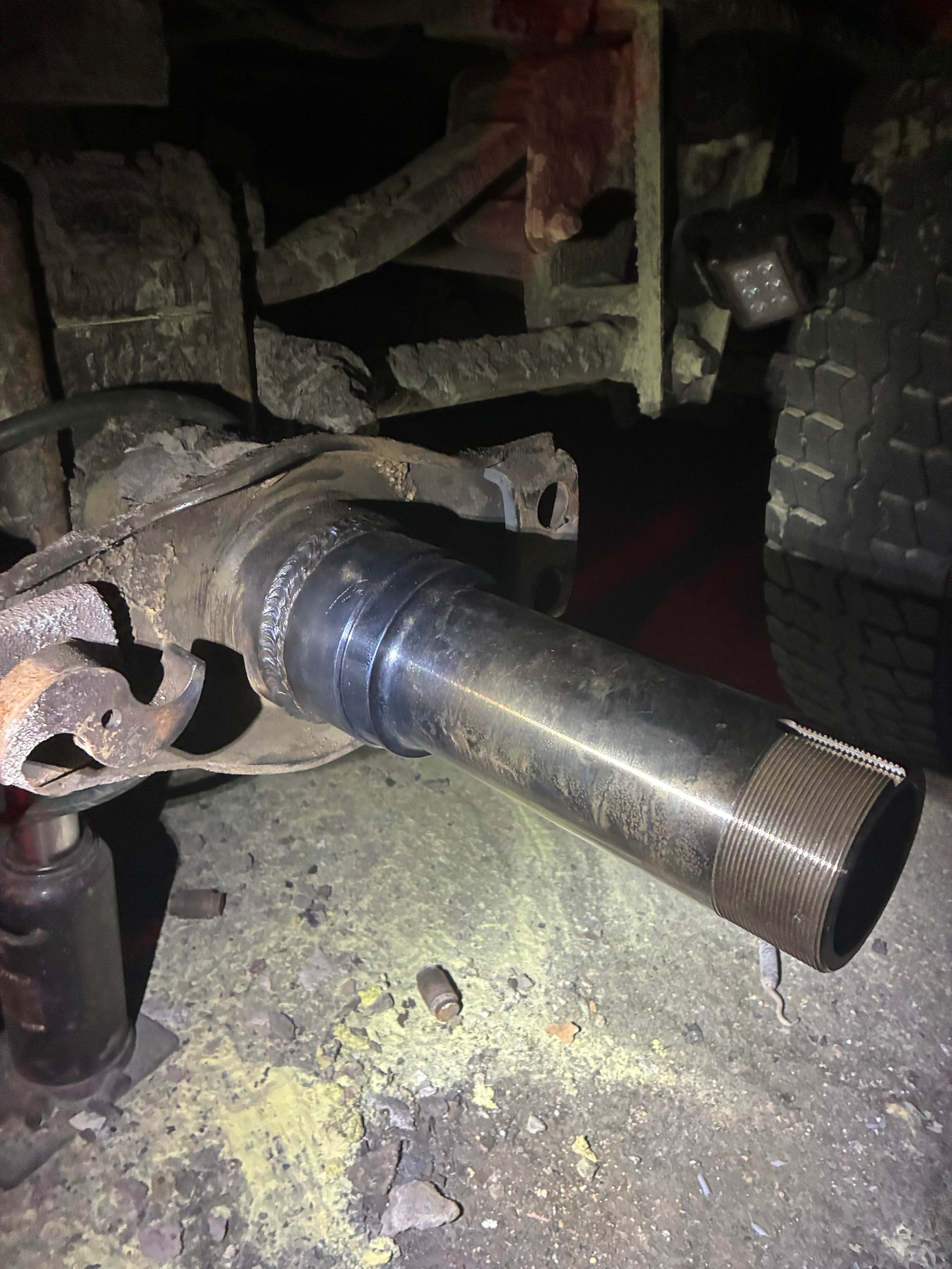 A detached truck axle with welded components and a threaded end.