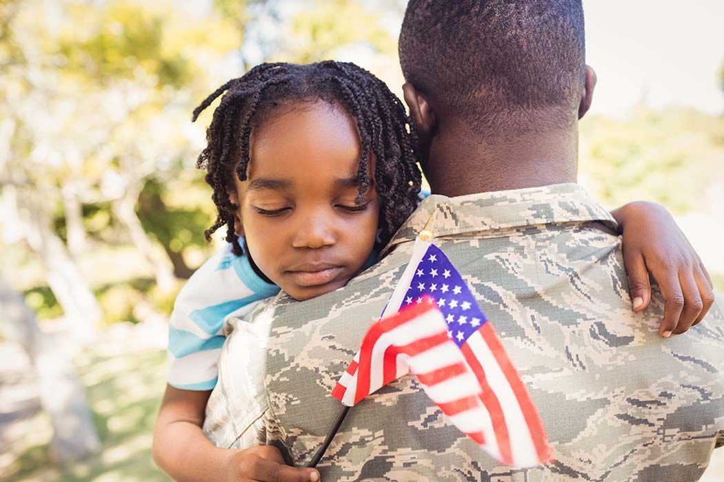 A little girl is hugging a soldier with an american flag on his back.