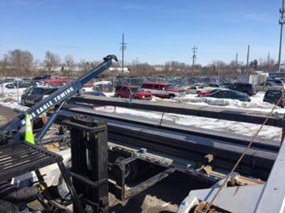 Tow truck at a junkyard, with rows of wrecked cars in the background under a blue sky.