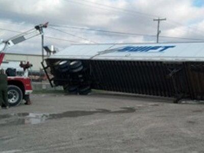 A semi-truck trailer on its side, being uprighted by a tow truck, with the Swift logo visible.