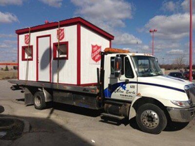 A Salvation Army donation booth being transported on a tow truck. The booth is white with red trim and logos.