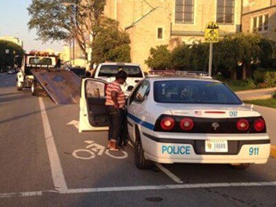 A police car and tow truck at the side of a road next to a bicycle lane. 