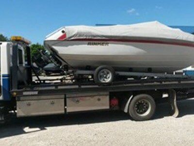A boat on a trailer loaded on a tow truck. The boat is covered and has red accents.