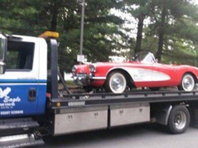 Red vintage Corvette being towed on a flatbed tow truck with 
