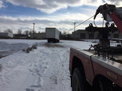 Tow truck pulling a box truck out of the snow. The scene is outdoors on a snowy day.