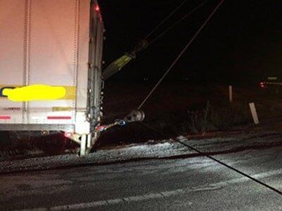 A semi-truck has snagged overhead wires, with the wires and supporting equipment pulled down towards the truck. It's nighttime.