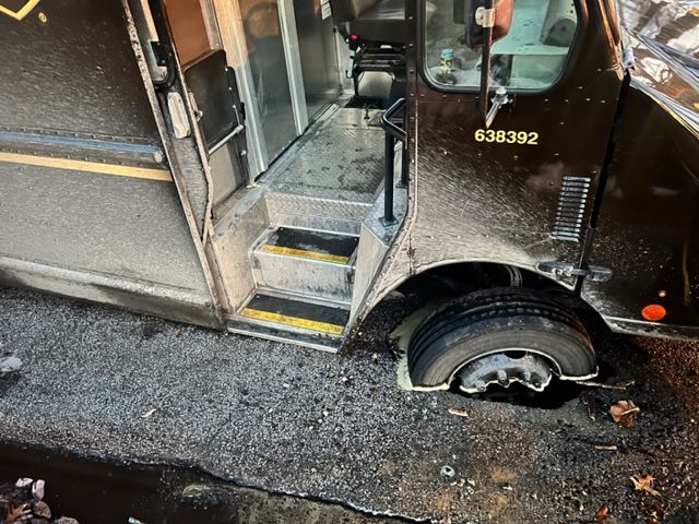 A damaged UPS delivery truck with a flat tire and visible collision damage on its side. 
