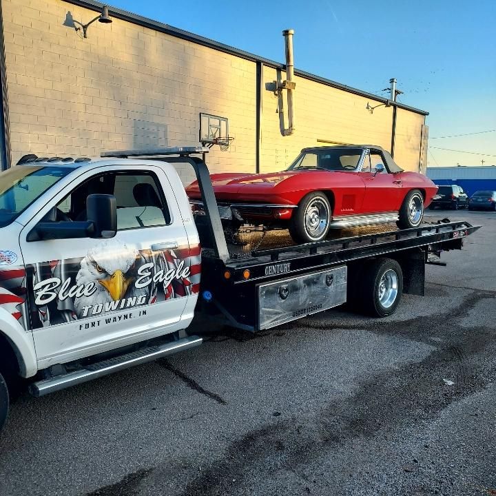 A red classic Corvette being towed by a white Blue Eagle Towing truck.