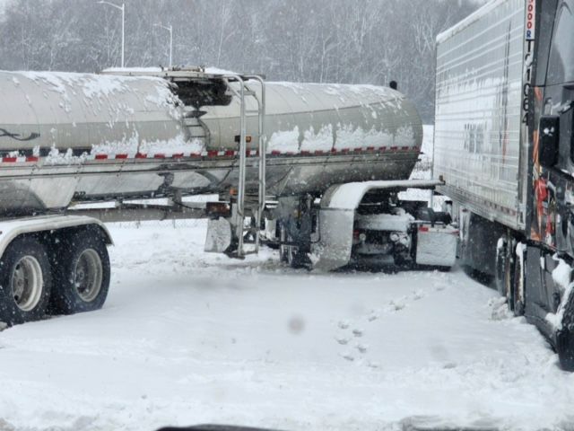 A tanker truck damaged in a snow-covered parking lot, next to a semi-truck.