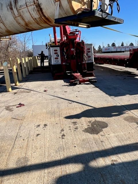 A tow truck lifting a large, cylindrical object in a paved lot. 