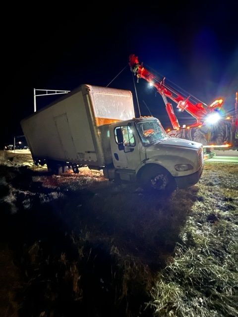 A white box truck is being pulled from a ditch by a red tow truck at night.