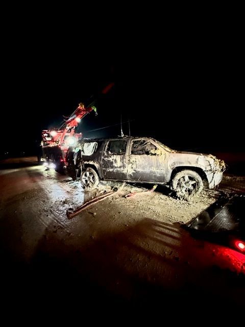 A tow truck pulling a heavily damaged SUV from the side of a dark road at night.