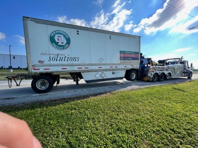 A semi-truck pulling a trailer on a roadside; the trailer has 
