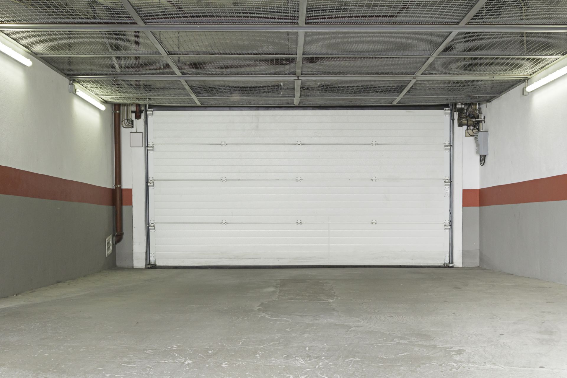 White garage door in a concrete room with a red stripe and metal ceiling.