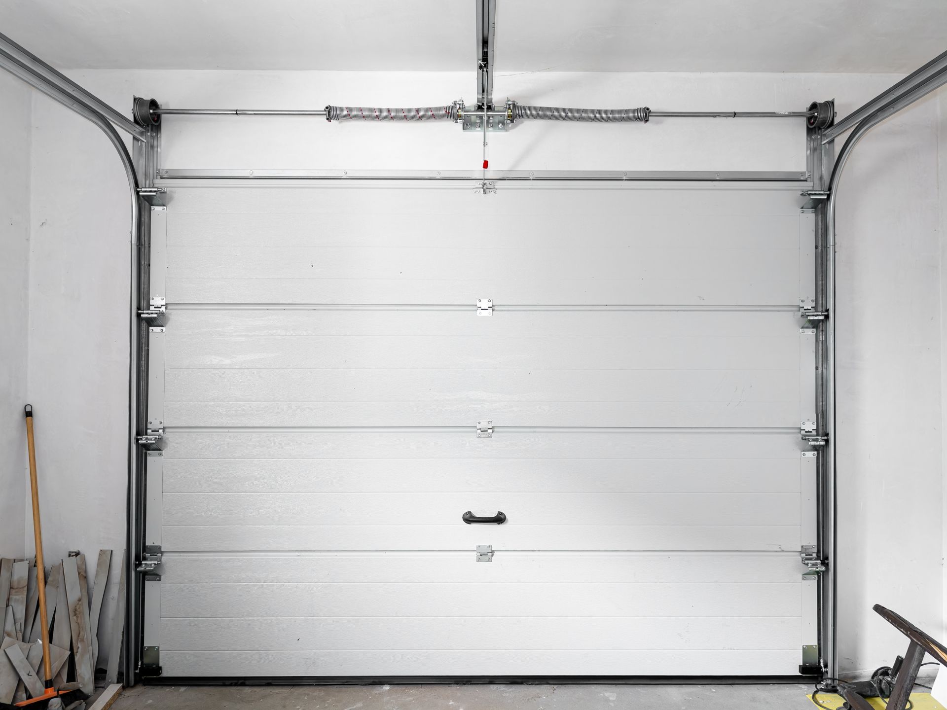 White garage door closed, with horizontal panels. Silver tracks and spring visible.