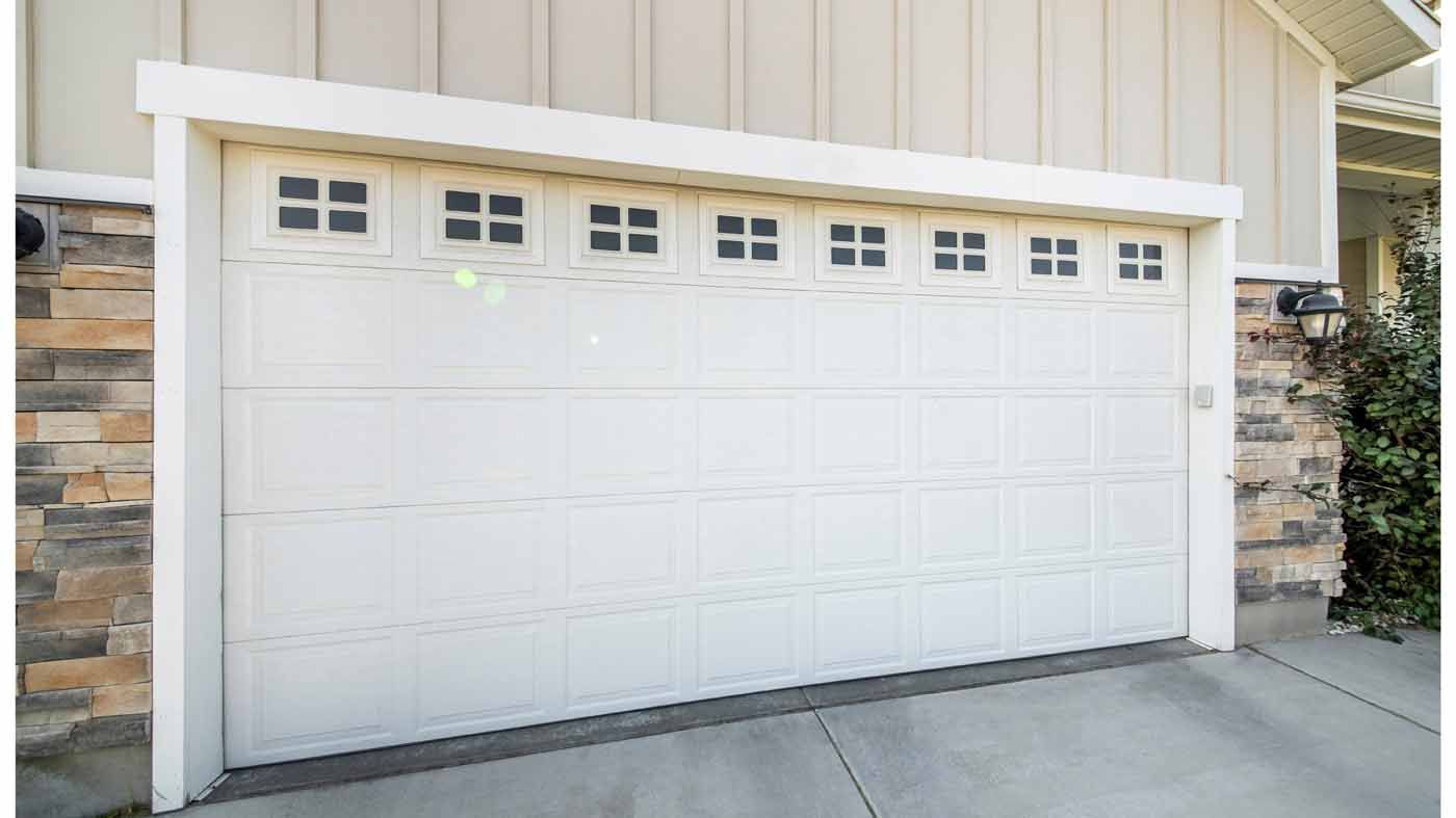 White garage door with small square windows in a home's exterior; stone and siding visible.