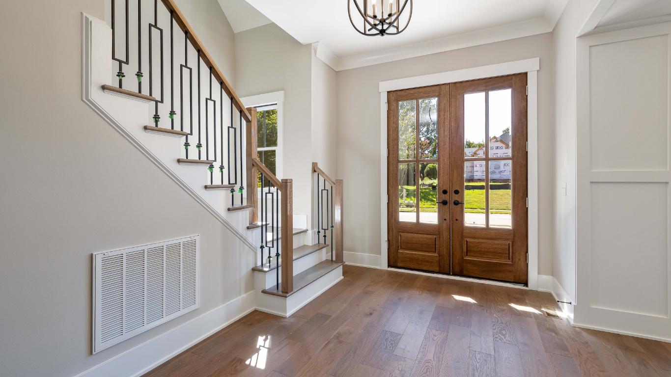 Entryway with wooden double doors, staircase, and hardwood floors. Light gray walls.