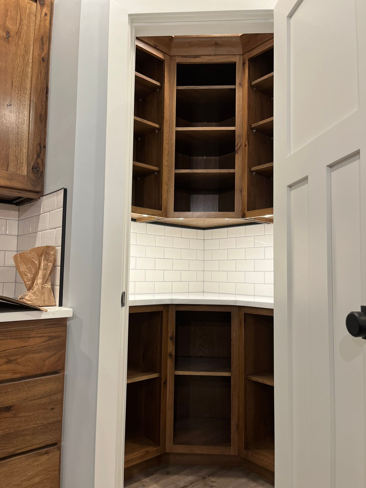 A walk-in pantry with wooden cabinets, white tile, and open white doors in a home.