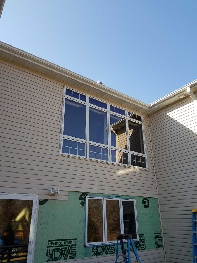 Beige house exterior with large multi-pane windows and exposed wall under construction.