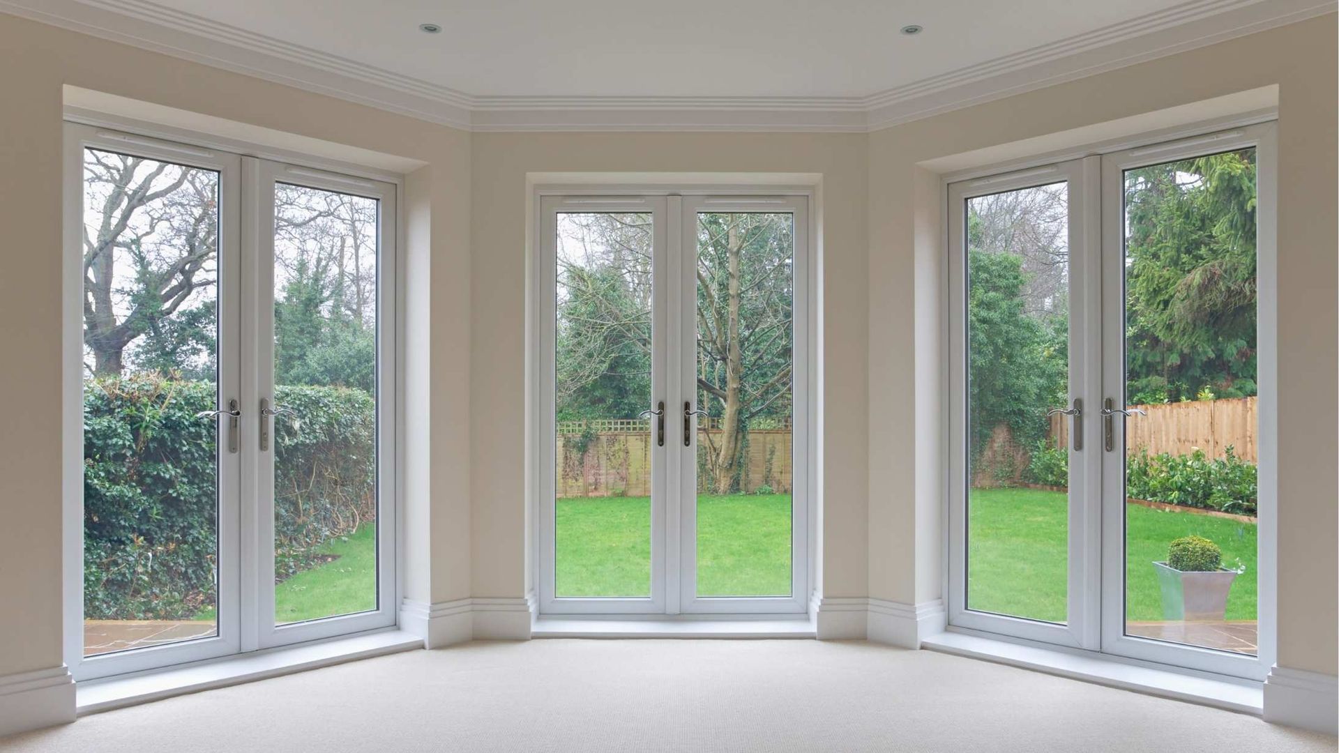 Room with three white framed glass doors looking onto a green lawn and garden.