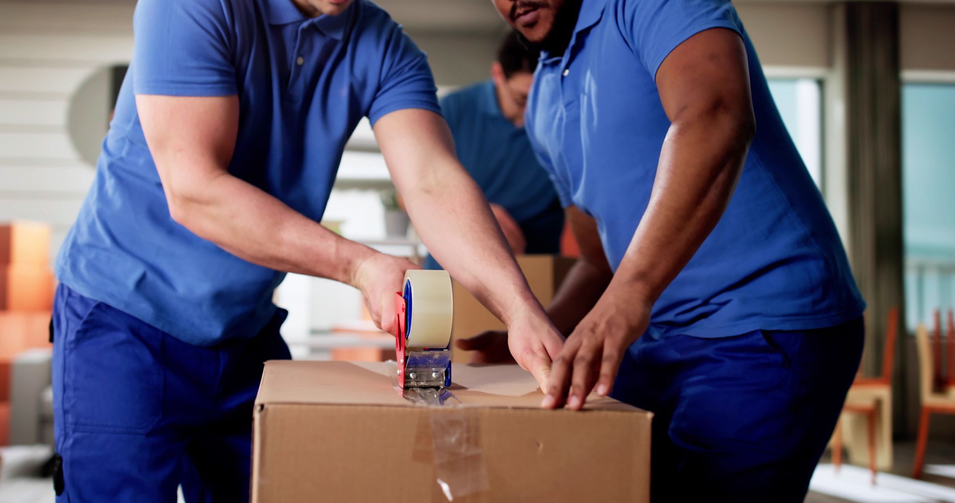Professional movers sealing a cardboard box during a residential move. Professional movers sealing a cardboard box during a residential move.