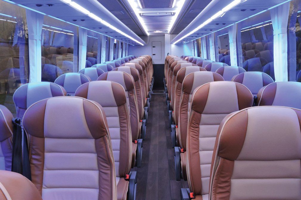 Interior view of a bus with rows of tan and brown seats, bathed in a cool blue light.