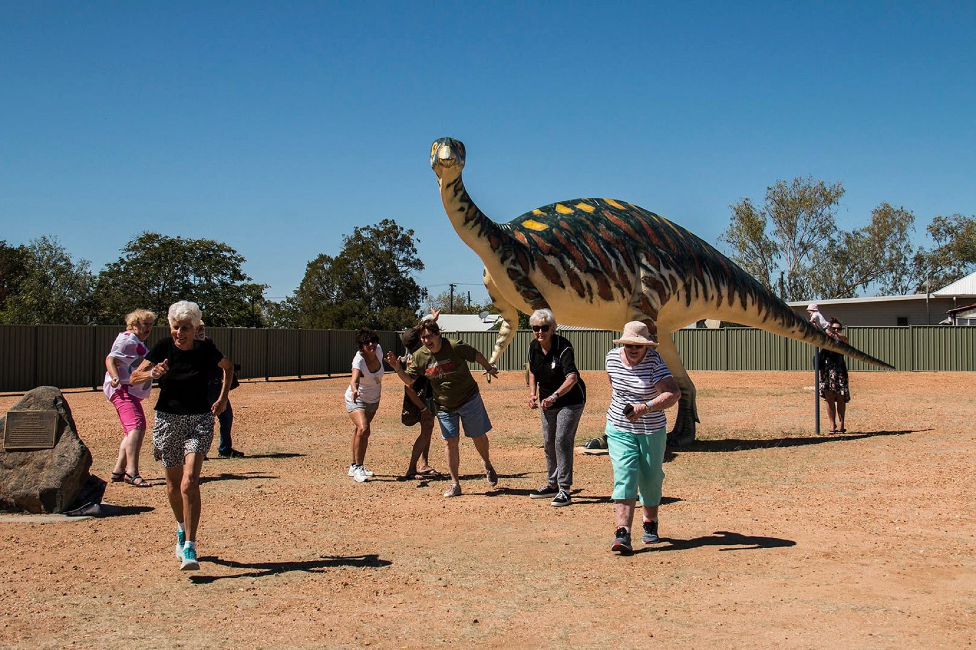 A group of people are standing in front of a large dinosaur statue.