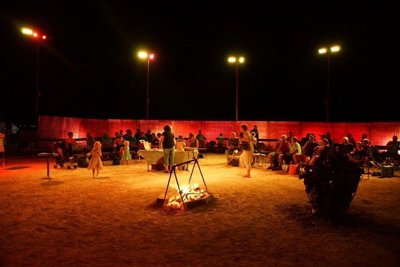 A group of people are standing around a fire pit at night.