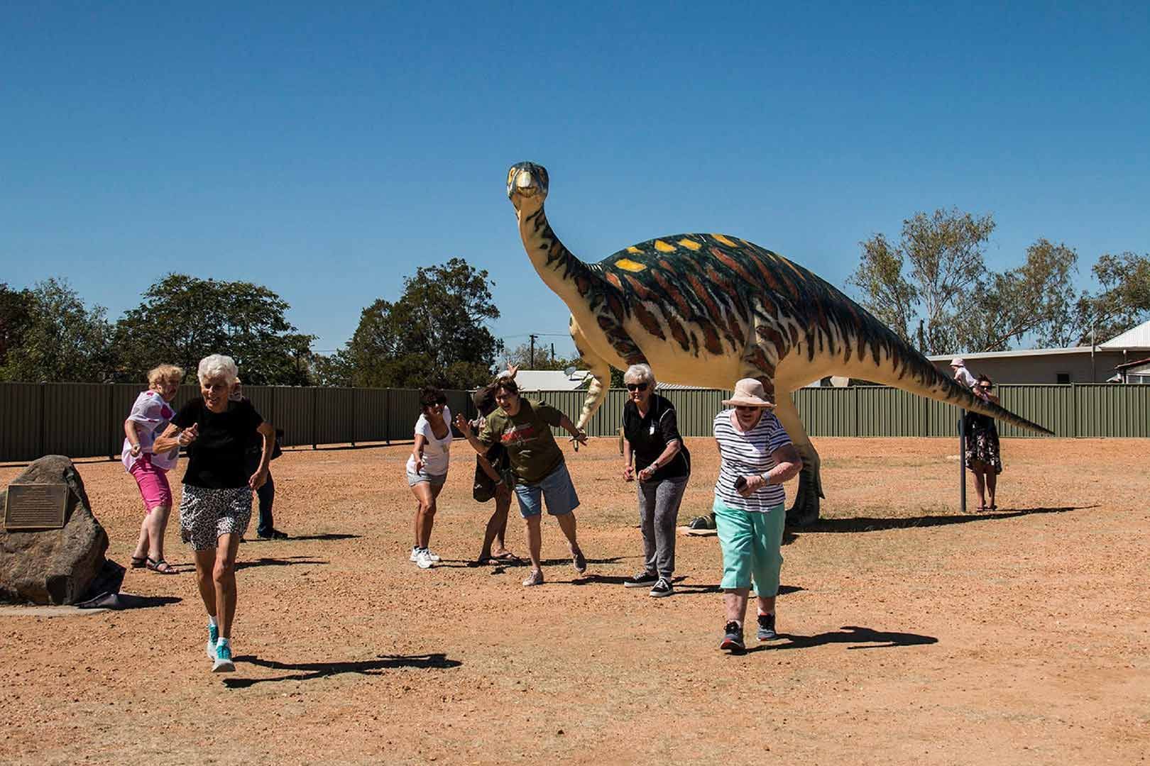 A Group of People Are Standing in Front of A Large Dinosaur Statue — G & D Ross Bus Charters In Magnolia, QLD