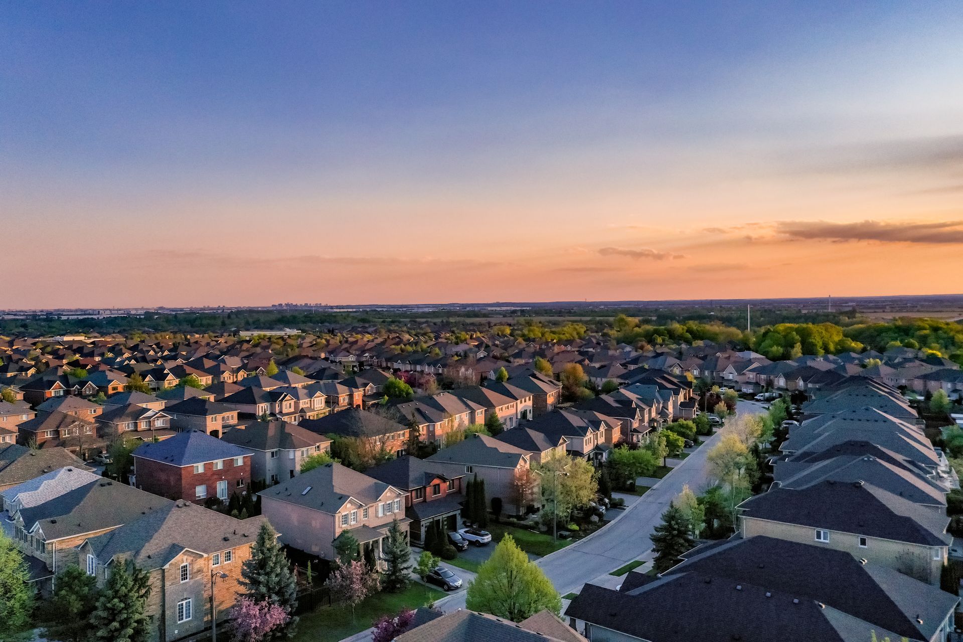 Aerial view of a suburban neighborhood at sunset with rows of houses and a colorful sky