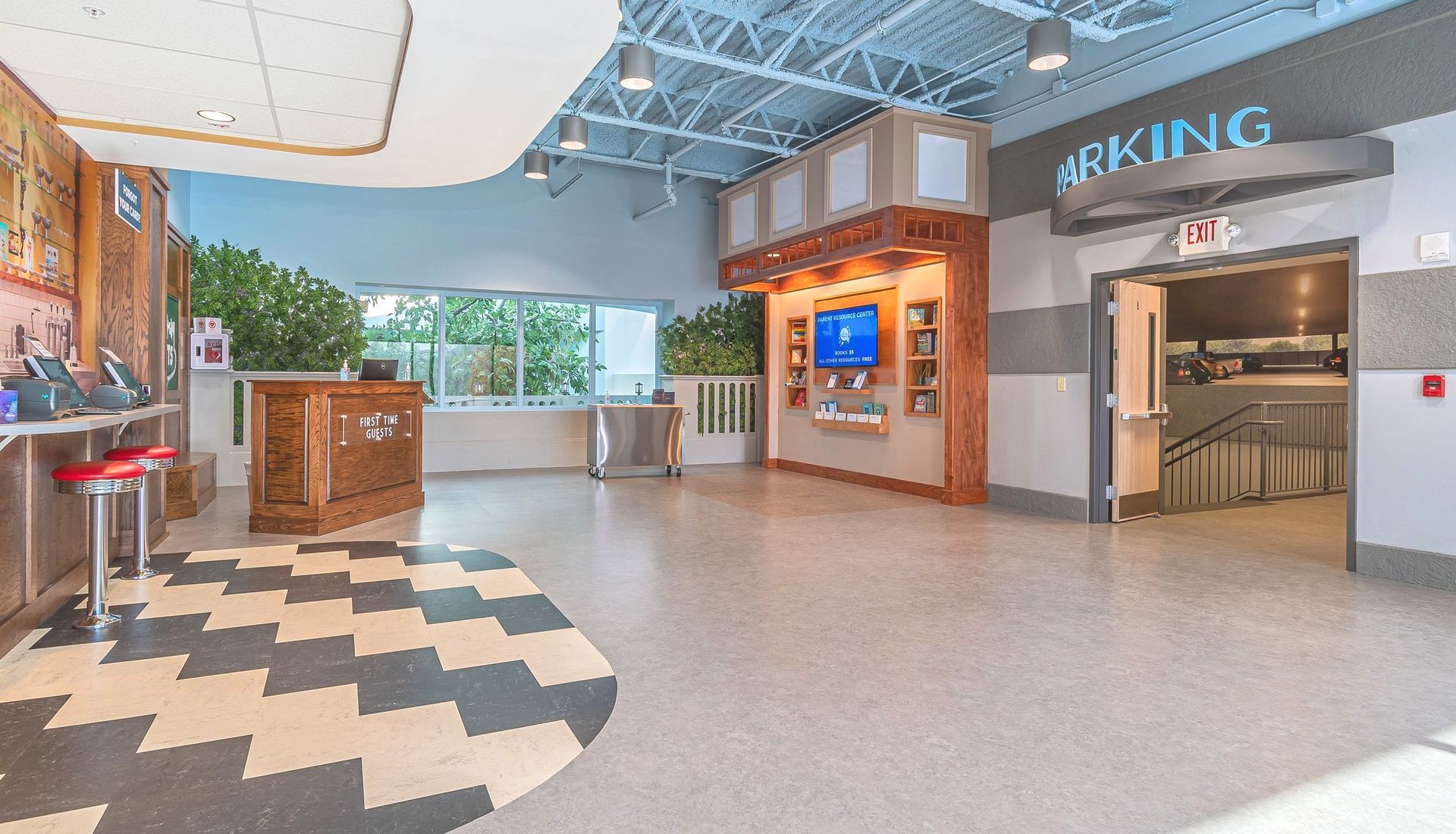 Spacious lobby with patterned floor, counter, parking entrance, and TV on a brick wall.