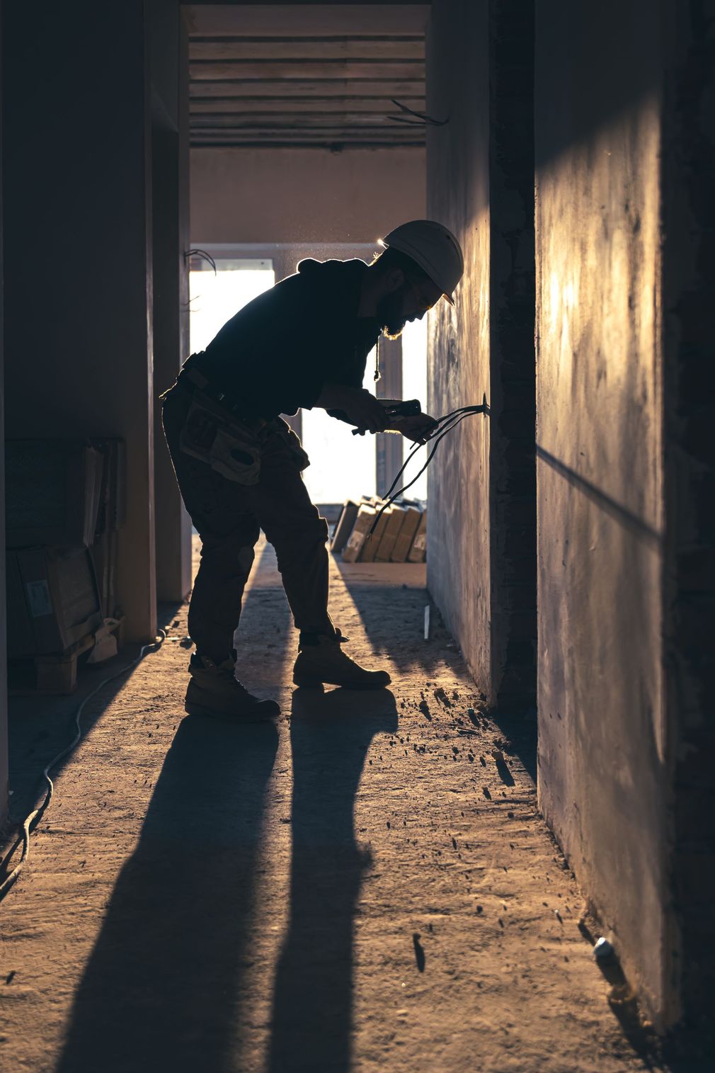 Silhouette of a construction worker wearing a hard hat, working on a wall in a hallway.