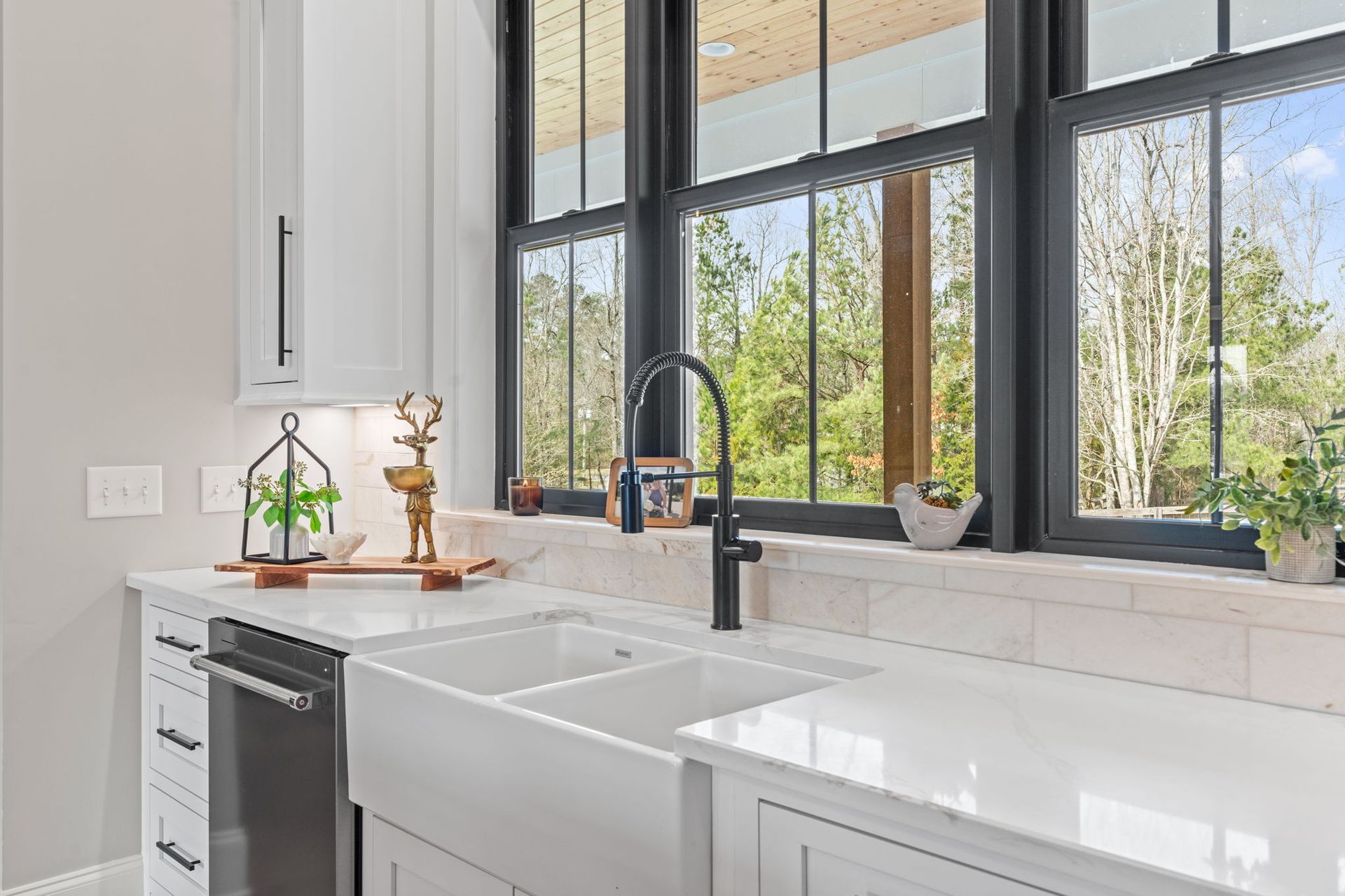 A kitchen with a sink , dishwasher , and large windows.