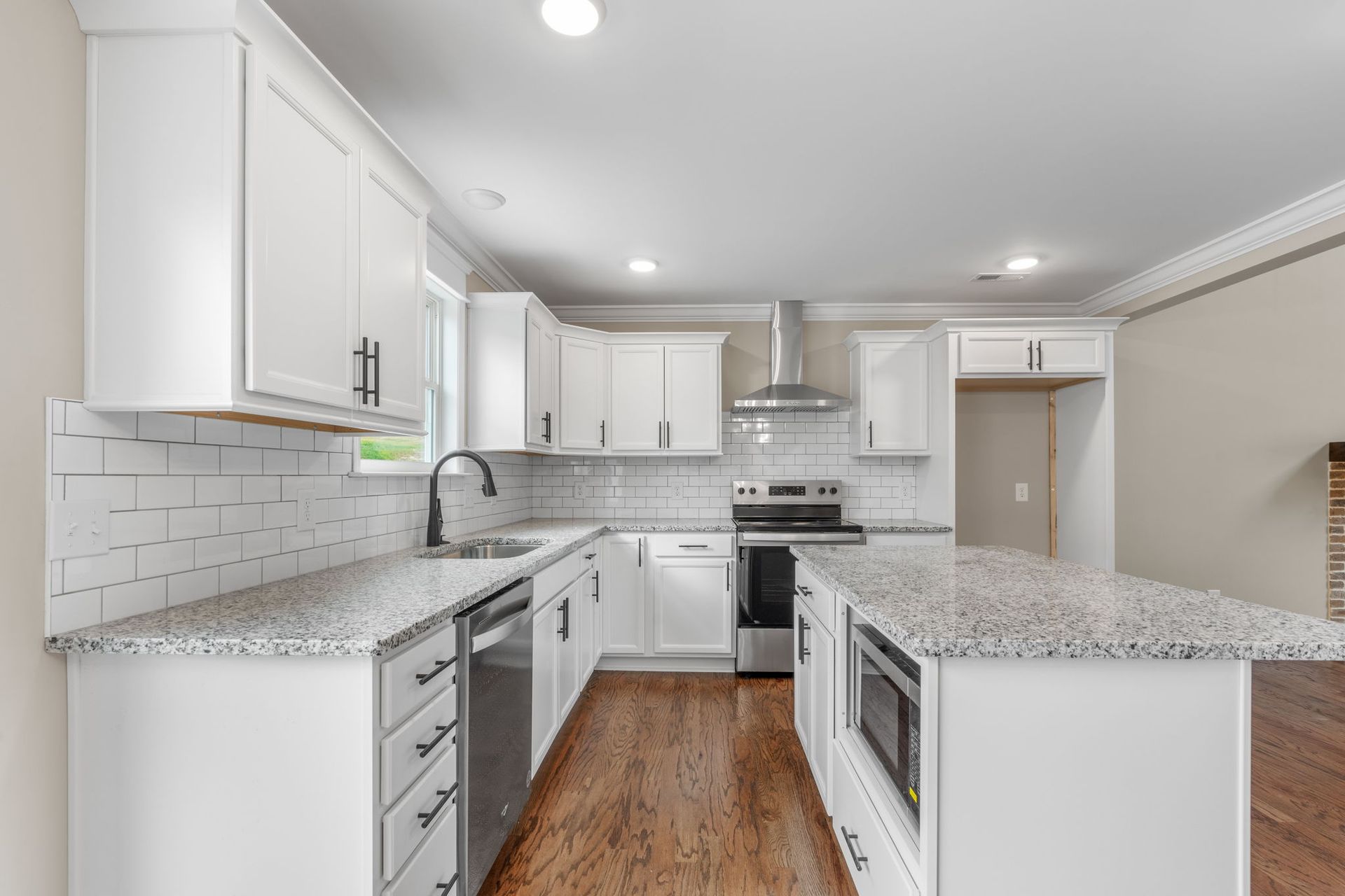 A kitchen with white cabinets , granite counter tops , stainless steel appliances and hardwood floors.