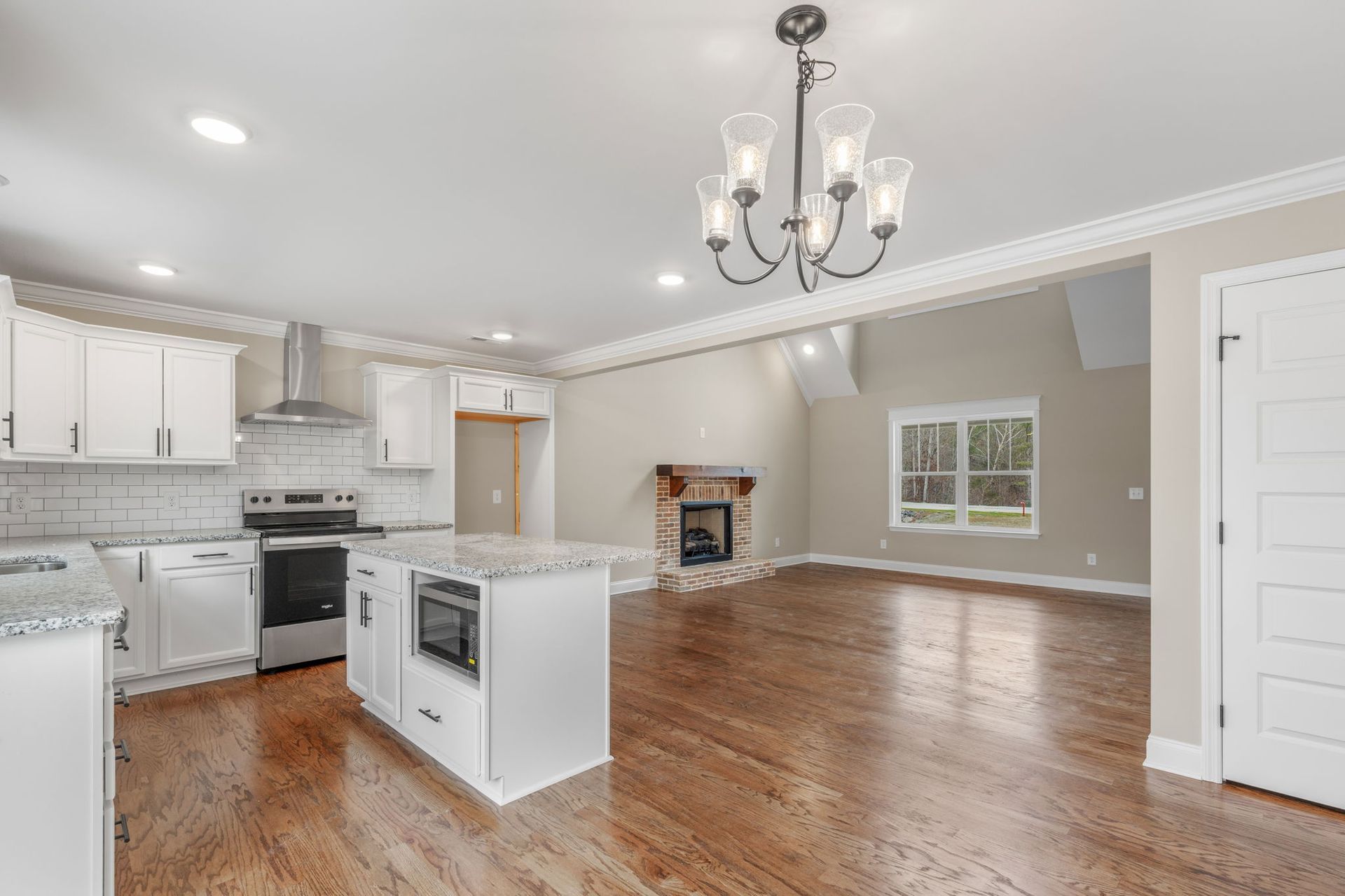 A kitchen with white cabinets , stainless steel appliances , hardwood floors and a chandelier.