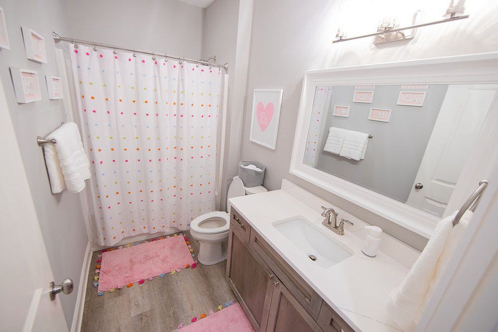 A bathroom with a toilet , sink , shower curtain and mirror.