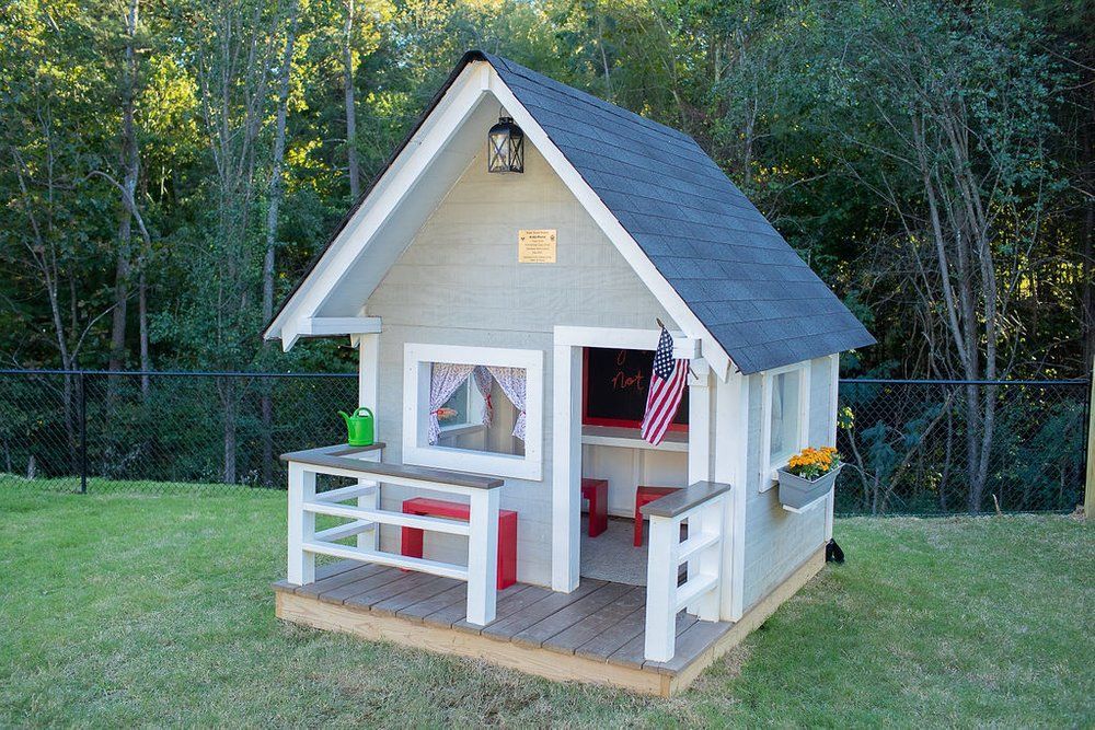 A small white playhouse with a gray roof is sitting on top of a lush green field.