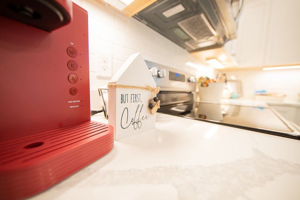 A red coffee maker is sitting on a kitchen counter next to a small wooden house.
