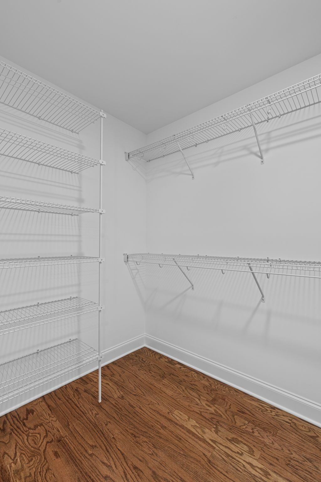 An empty walk in closet with wooden floors and white shelves.