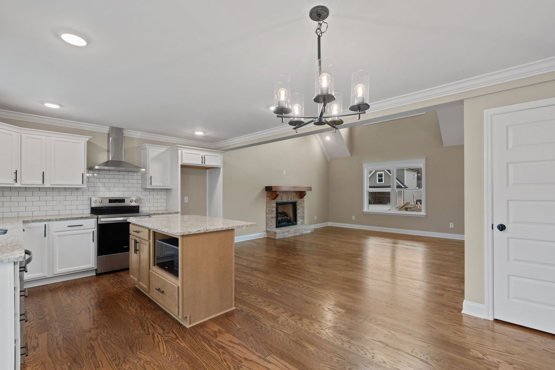 A kitchen and living room in a house with hardwood floors and a chandelier.