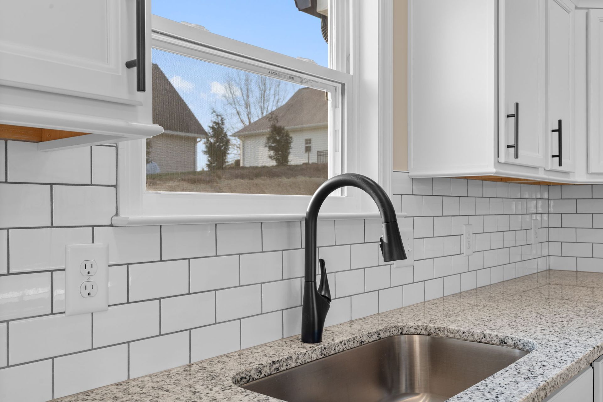 A kitchen with a sink and a window with a view of a house.
