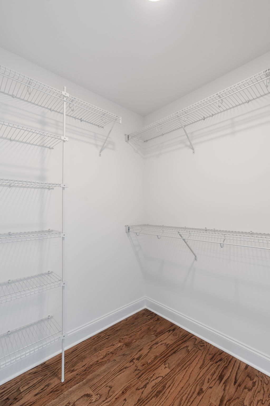 An empty walk in closet with hardwood floors and white shelves.
