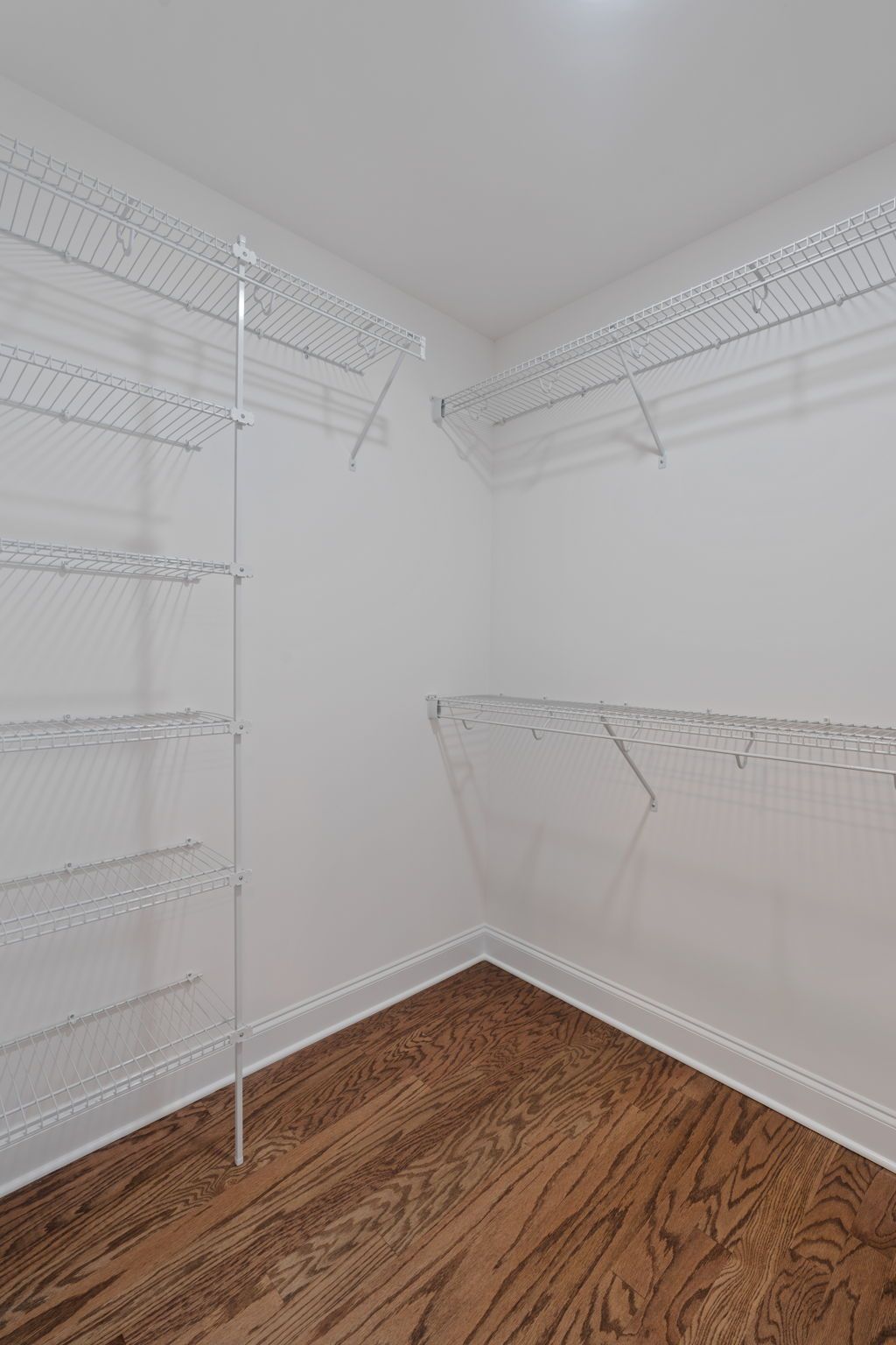 An empty walk in closet with hardwood floors and white shelves.